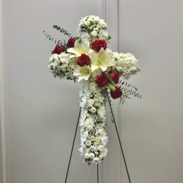 White floral cross on a stand with red roses and lilies