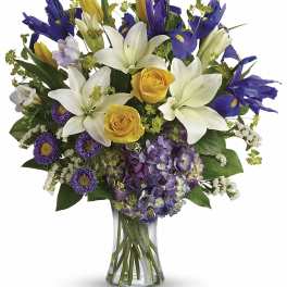 Bouquet of white lilies, yellow roses, purple irises, and hydrangea in a glass vase