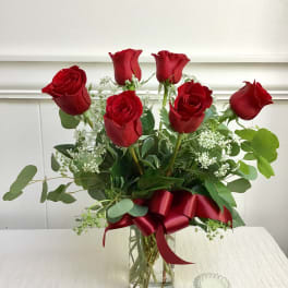 Red roses arranged in a clear glass vase with a red ribbon