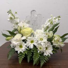 White floral arrangement with daisies and roses around a clear angel figurine