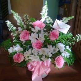 Pink roses and white flowers in a basket with a pink ribbon and envelope card