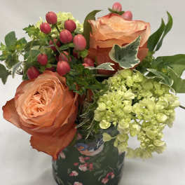 Peach roses with pink berries and pale green hydrangeas in a patterned vase