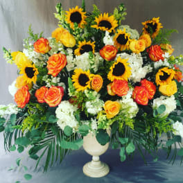 Large bouquet of sunflowers, roses, and white flowers in a cream urn vase