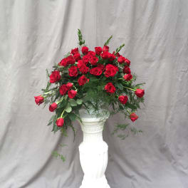 Red roses arranged in a tall white pedestal vase