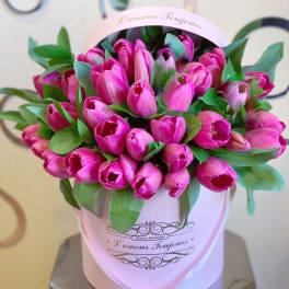 Pink tulips arranged in a round pink hatbox with green leaves