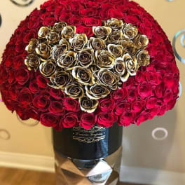 Large dome of red roses with a gold rose heart in a black hatbox on a tall pedestal.