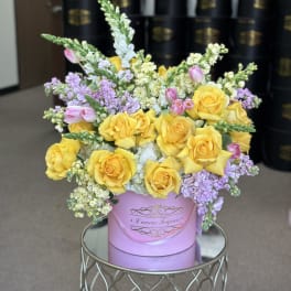 Yellow roses and lavender flowers arranged in a pink hat box