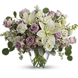 Lavender roses and white lilies arranged in a clear glass vase
