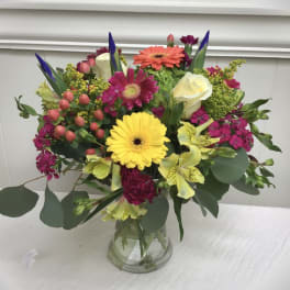 Bright mixed bouquet of gerbera daisies, roses, and other blooms in a clear glass vase