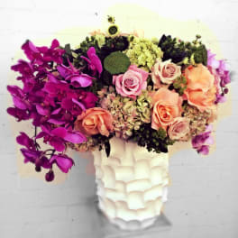 Mixed bouquet of orchids, roses, and hydrangeas in a white vase