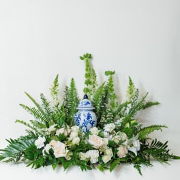 White roses and greenery arranged around a blue-and-white ceramic urn