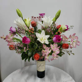 Bouquet of lilies, roses, and pink alstroemeria in a wine bottle vase