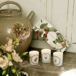 Lit candles beside a ceramic jug and a floral box