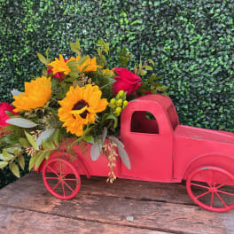 Pink toy truck filled with sunflowers and red roses