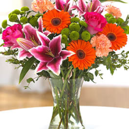 Mixed bouquet of pink lilies, orange gerbera daisies, roses and carnations in a clear glass vase