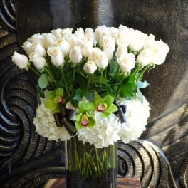 White roses and green orchids in a tall glass vase
