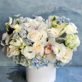 White and pale blue floral arrangement in a white vase