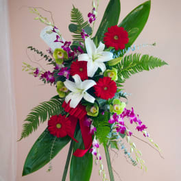 Standing floral spray with red gerberas, white lilies, and purple orchids