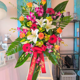 Tall standing floral spray with lilies, gerbera daisies, roses, and orchids on an easel