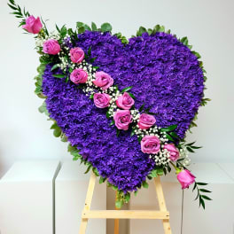 Heart-shaped purple floral arrangement with pink roses on an easel