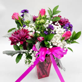 Pink roses and purple flowers in a pink vase with a ribbon