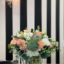 Peach roses and succulents arranged in a clear glass bowl vase