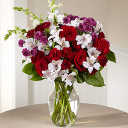 Bouquet of red roses, white alstroemeria, and purple carnations in a glass vase
