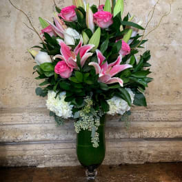 Pink roses and lilies arranged in a tall green glass vase