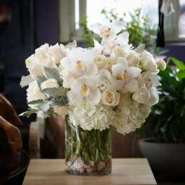 White floral arrangement in a glass vase with orchids and roses