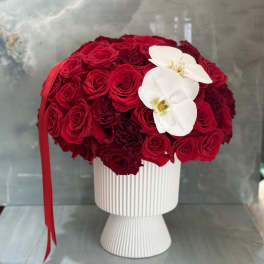 Red rose arrangement in a white pedestal vase with two white orchids