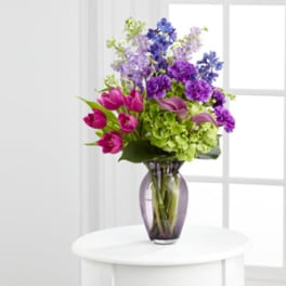Mixed bouquet of purple, pink, and green flowers in a glass vase