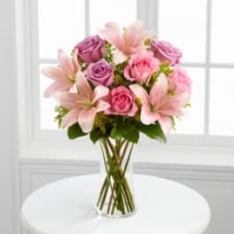 Pink lilies and roses arranged in a clear glass vase