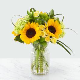 Sunflowers and pale yellow roses arranged in a clear glass vase