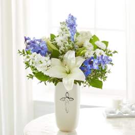 White lilies and blue-white flowers in a cream vase with a cross emblem