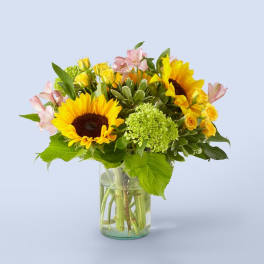 Bouquet of sunflowers, yellow roses, and pink flowers in a glass vase