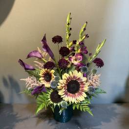 Purple calla lilies and sunflowers in a dark vase