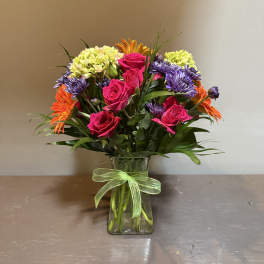 Mixed bouquet of pink roses, purple daisies, and orange blooms in a glass vase
