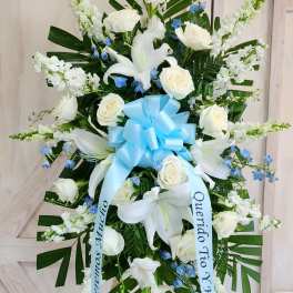 Standing funeral spray of white lilies and roses with blue accents and a ribbon