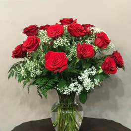 Red roses arranged in a clear glass vase with white filler flowers
