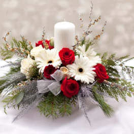 Red roses and white daisies arranged around a white pillar candle