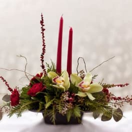 Red candle centerpiece with orchids and greenery in a low container
