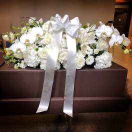 White floral casket spray with orchids, roses, and a large satin bow