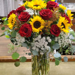 Bouquet of red roses and yellow sunflowers in a clear glass vase
