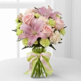 Pink lilies and roses in a glass vase with a ribbon