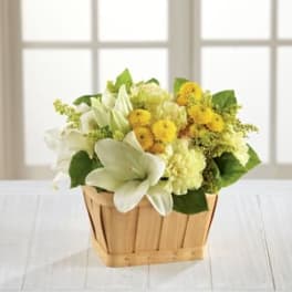 White lilies and yellow flowers arranged in a wooden basket