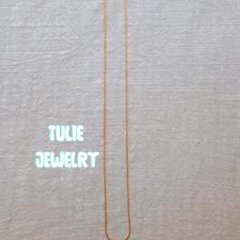 A thin gold necklace laid flat on a light fabric background.