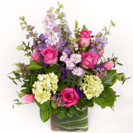 Pink roses and purple flowers arranged in a glass vase
