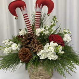 Holiday floral arrangement with red roses, white blooms, pinecones, and elf decorations