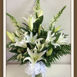 White lilies arranged in a glass vase with a white ribbon bow