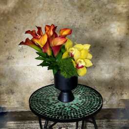 Arrangement of red-orange calla lilies and yellow orchids in a black vase